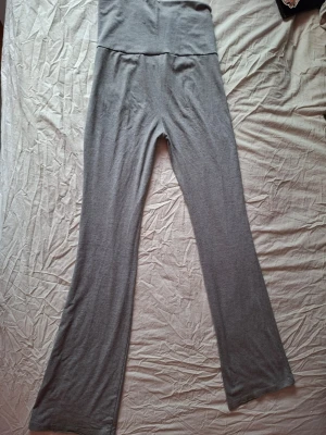 Grå mjuka loungebyxor - Ett par grå loungebyxor i mjukt och stretchigt material. Byxorna har hög midja och raka ben med avslappnad passform, perfekta för hemmamys eller chill dagar. Inga synliga fickor eller detaljer. Märke och material är ej angivet.