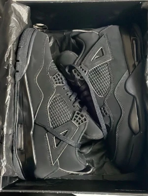 Svarta Air Jordan 4 Black cats - Säljer ett par helsvarta Air Jordan 4 Retro sneakers med ikoniska meshpaneler och detaljer i läder och syntet. Skorna har en chunky sula med synlig Air-enhet och Jumpman-logga på plösen. Perfekta för dig som vill ha en clean och klassisk look. KVITTO FINNS