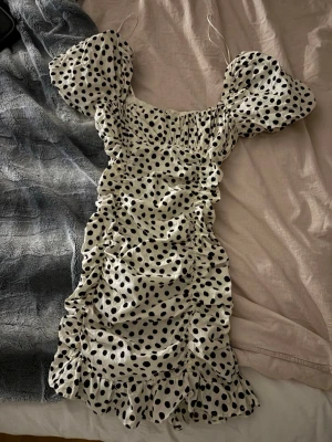Prickig kortklänning från Zara - Supersöt vit kortklänning från Zara med svarta prickar, puffärmar och rynkade detaljer längs sidorna, klänningen har även en volangkant nertill