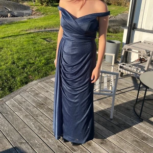 Mörkblå, glittrig balklänning - Vacker, mörk blå balklänning med vackert släp som tindrar i solen! Endast använd en gång. Passar i låga klackar för mig som är 160 . Storlek 42, passar mig som brukar ha från M till L. Hör gärna av er om ni har frågor kring mått eller vill ha några fler bilder eller liknande 💕nypris 4000 kr. Påse ingår. 