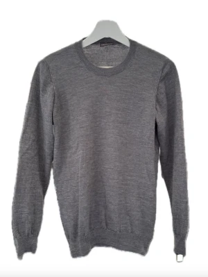 Grå stickad tröja med rund hals - En stilren grå stickad tröja med rund halsringning och långa ärmar. Tröjan har ribbade muddar vid ärmslut och nederkant. Perfekt för lager på lager och enkel att matcha med olika outfits. Materialet ser ut att vara mjukt och bekvämt.