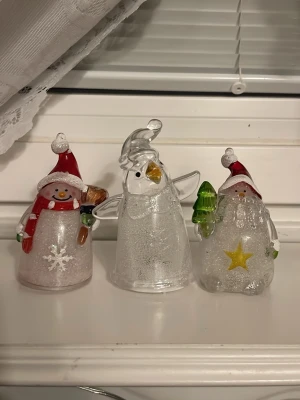 Glasfigurer med LED-belysning julmotiv - Tre dekorativa glasfigurer med LED-belysning i form av snögubbe, pingvin och tomte. Figurerna har detaljer i rött, grönt och gult samt glittereffekt. Perfekta som juldekorationer i fönster eller på hylla. Drivs av batteri och lyser i olika färger.