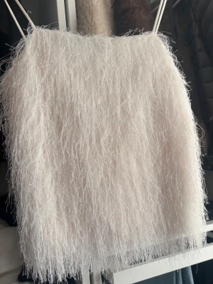 Vit fluffig linnetopp med tunna band - Supersöt vit linnetopp med tunna axelband och fluffig, pälsliknande textur. Perfekt för dig som vill sticka ut med en unik och trendig look. Toppen är ärmlös och har en croppad passform som ger en modern vibe.