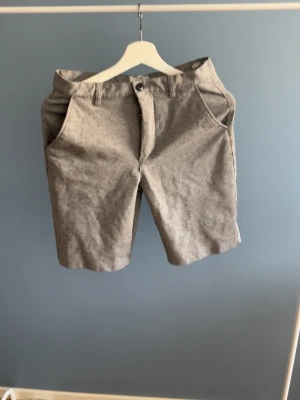 Gråa shorts med fickor - Snygga grå shorts med normal passform och klassisk design. Shortsen har två sidofickor fram och två bakfickor med knapp. Perfekta för sommaren och tillverkade i ett mjukt bomullsmaterial. Stängs med knapp och dragkedja.