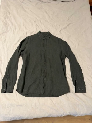 Massimo Dutti Linneskjorta  - Stilren mörkgrön skjorta från Massimo Dutti i 100% linne. Skjortan har klassisk krage, långa ärmar och knappar framtill samt vid ärmsluten. Perfekt för dig som gillar en enkel men snygg look.