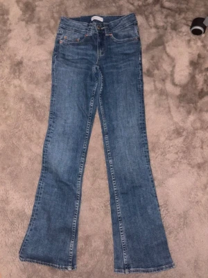 Blå bootcut jeans med fickor från Gina Tricot - Ett par klassiska blå bootcut jeans med snygga bakfickor och knappar. Jeansen har normal midja och är tillverkade i denim med lätt tvättad look. Perfekt för dig som gillar en avslappnad och trendig stil.