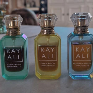 Kayali parfym trio mini - Säljer ett set med tre Kayali parfymer i miniflaskor: Maui in a Bottle Sweet Banana, Capri in a Bottle Lemon Sugar och Maldives in a Bottle Ylang Coco. Flaskorna är i glas med färgerna turkos, gul och blå, och har eleganta, facetterade lock i plast med gulddetaljer.