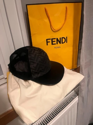 Svart keps från Fendi med meshdetaljer - Snygg svart keps från Fendi med klassiskt FF-mönster framtill och meshpaneler på sidorna för extra ventilation. Justerbar baktill för perfekt passform och böjd skärm i svart. Perfekt accessoar för dig som gillar exklusiv streetwear.
