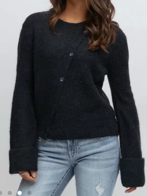 Marinblå kofta med knappar - Mysig marinblå kofta med knäppning framtill och stora uppvikta muddar på ärmarna. Koftan har en avslappnad passform och är stickad i ett mjukt material som ger en trendig look. Perfekt att matcha med jeans för en cool vardagsstil.