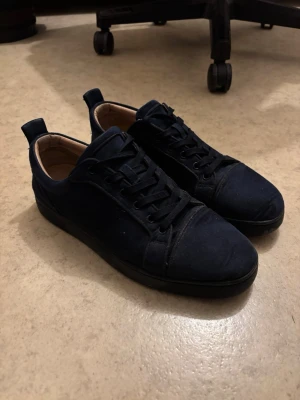 Mörkblå sneakers från Christian Louboutin - Snygga mörkblå sneakers från Christian Louboutin med klassisk röd sula och diskret logga undertill. Skorna har ovandel i mocka, svarta skosnören och låg profil. Perfekta för dig som vill ha en stilren och exklusiv look. Skolåda finns osv. Sparsamt och sällan använda över ca 1,5 års tid utan några märkbara skador. Kom med prisförslag och frågor.