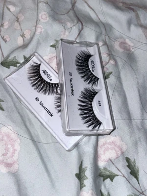 Ardell 3D Faux Mink Lösögonfransar - Säljer två par Ardell 3D faux mink lösögonfransar i svart. Fransarna har en fyllig och fluffig design som ger volym och längd till dina ögon. De kommer i genomskinliga plastförpackningar och är tillverkade av syntetiskt material som efterliknar mink.