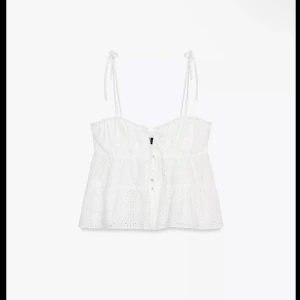 Vit broderad linnetopp med knytband - Superfin vit linnetopp med broderade detaljer och knytbara axelband. Toppen har knappar framtill och är lätt utsvängd nertill. Perfekt för varma dagar och ger en romantisk känsla till outfiten.