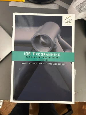 iOS Programming 4th Edition - iOS Programming: The Big Nerd Ranch Guide, 4th Edition av Christian Keur, Aaron Hillegass & Joe Conway. Boken har ett modernt omslag i svart, grått och grönt med tekniskt motiv. Perfekt för dig som vill lära dig apputveckling för iOS.