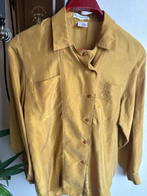 Gul silkesskjorta från Kurt Kellermann - Snygg gul skjorta i 100% silke från Kurt Kellermann. Skjortan har klassisk krage, knappar framtill och två bröstfickor, varav en med diskret broderi. Långärmad och med en lyxig, mjuk känsla som passar perfekt till din stil. Sold as seen, se wear and tear.💕