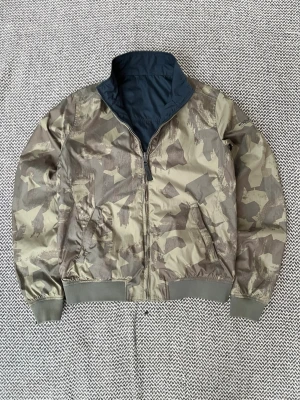 Marinblå/Khaki Woolrich Reversible vindjacka i storlek XS - Marinblå/khaki färgad Woolrich Reversible vindjacka i militärmönster Liten defekt Storlek 14 (motsvarar XS-S) Hör av er vid frågor!