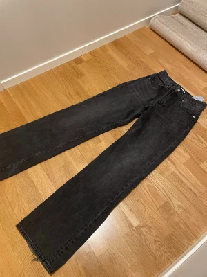 Svarta raka jeans från Zara - Säljer ett par svarta raka jeans från Zara med klassisk femficksmodell och hög midja. Jeansen är tillverkade i kraftigt denimtyg och har en snygg tvättad finish. Perfekta till sneakers eller boots för en avslappnad look.