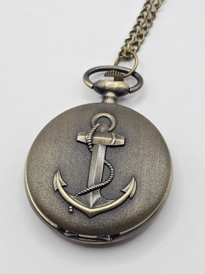 Kedjeförsedd fickur med ankare "klocka" - Snyggt fickur i antikbrons med kedja och ett detaljerat ankare i relief på locket. Uret har en rund form och en klassisk vintagekänsla, perfekt för dig som gillar marina detaljer och retrostil.