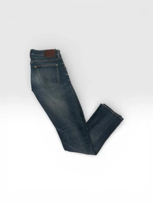 Blå jeans från Lee med raka ben - Säljer ett par klassiska blå jeans från Lee med raka ben och snygg slitning. Jeansen har fem fickor, Lee-lapp i brunt läder baktill och är gjorda i slitstark denim. Perfekta för en avslappnad och cool stil.