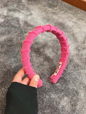 Rosa diadem från Lexi UF - Säljer ett rosa diadem från Lexi UF med coola råa kanter och tyg i lager på lager. Diademet har en trendig och ungdomlig look, perfekt för att lyfta vilken outfit som helst. Materialet är tyg och färgen är stark rosa. Super super skick. 