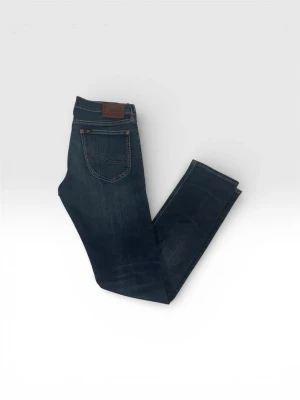 Mörkblå jeans från Lee - Snygga mörkblå jeans från Lee med klassisk femficksdesign och bruna sömmar. Jeansen har en rak passform och är tillverkade i slitstarkt denimtyg. Perfekta för dig som gillar en tidlös och enkel stil.