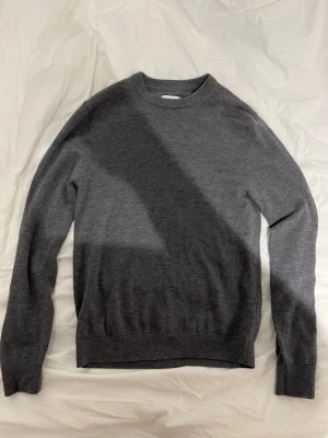 Mörkgrå stickad tröja - Stickad mörkgrå tröja i merinoull från These Glory Days. Säljer för att den blivit för lite för mig. Använd bara ett fåtal gånger.