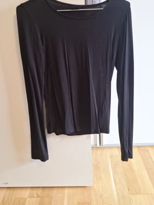 Svart långärmad topp Gina Tricot - En enkel och stilren svart långärmad topp från Gina Tricot. Modellen har rund halsringning och är figurnära i passformen. Perfekt att matcha med jeans eller kjol för en clean look.