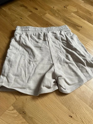Ljusgrå bomullsshorts med resårmidja - Säljer ett par ljusgrå shorts i mjuk bomull med elastisk midja. Perfekta för chill dagar eller träning. Klassisk passform och enkel design utan synliga loggor eller detaljer.