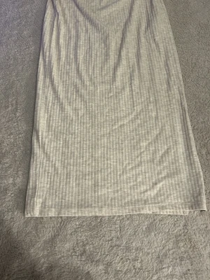 Beige ribbad kjol från ONLY - Säljer en beige, ribbad kjol från ONLY i storlek S. Kjolen är midilång med smal passform och har ett diskret randigt mönster i tyget. Perfekt att styla med en crop top eller oversized tröja för en chill look.