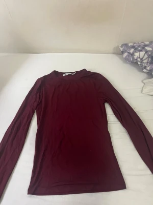 Mörkröd långärmad topp - En enkel och stilren mörkröd långärmad topp med rund hals. Perfekt att matcha med jeans eller kjol för en clean look. Tunn och mjuk i materialet, sitter tight mot kroppen.