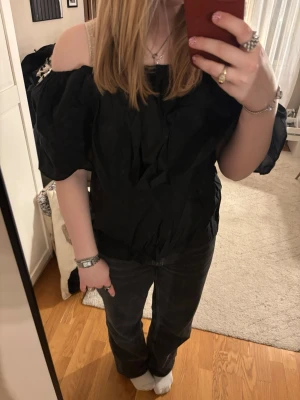 Svart offshoulder blus från Copenhagen Muse - Säljer en svart offshoulder blus från Copenhagen Muse. Blusen har en bred volang runt axlarna och är tillverkad i ett lätt tyg som ger en luftig känsla. Perfekt för dig som gillar en trendig och avslappnad stil.