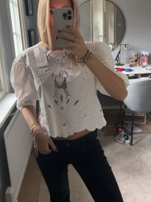 Vit broderad blus med puffärm - Trendig vit blus med broderade detaljer och hålmönster. Puffiga trekvartsärmar och rak, något kortare passform. Blusen har rund halsringning och vågig nederkant. Perfekt för en stilren och modern look. Storlek L men sitter som en S