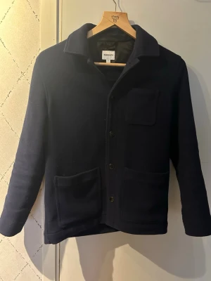 Mörkblå overshirt från Kappahl  - Stilren mörkblå overshirt från Kaphall med klassisk krage och tre fickor framtill. Overshirten har knäppning med svarta knappar och är tillverkad i ett mjukt, tjockare tyg som passar perfekt som lager. Enkel och clean design som funkar till många olika stilar.