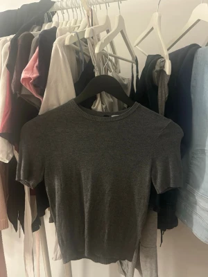 Mörkgrå stickad kortärmad topp - En enkel och stilren mörkgrå stickad topp med rund hals och korta ärmar. Perfekt att matcha med både jeans och kjol för en clean look. Mjuk och bekväm, passar dig som gillar minimalistisk stil.