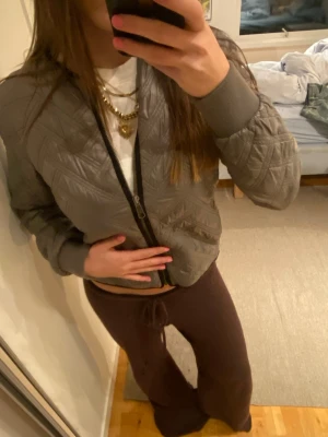 Grå vårjacka  - Snygg grå bomberjacka med quiltat mönster och ribbade muddar. Jackan har dragkedja framtill och en klassisk bomberkrage. Perfekt för dig som vill ha en stilren och trendig look. Materialet känns mjukt och bekvämt.