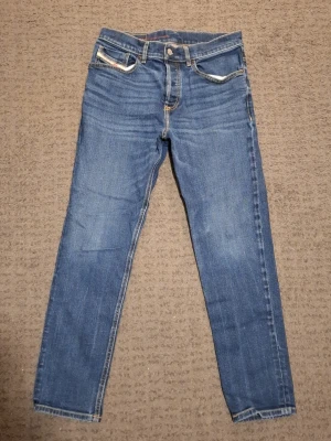 Blåa Diesel jeans - Säljer ett par blåa Diesel jeans med passform regular och fem fickor. Jeansen har 28W 32L och kontrastsömmar. Jeansen har en tidlös look. Perfekta för dig som gillar enkel och stilren stil. Köpt från åhlens för 1300 kr