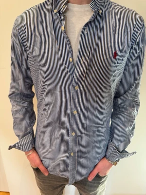 Blå vit randig Ralph Lauren skjorta - Säljer en riktigt snygg blå vit randig Ralph Lauren skjorta i storlek S. Modellen på bilden är 173 cm lång och väger 62 kg.