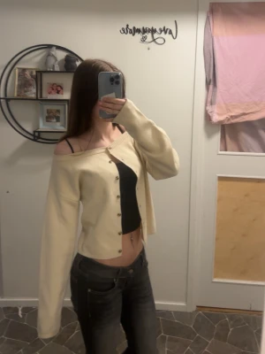 Krämvit cardigan från H&M - Trendig krämvit cardigan från H&M med knappar framtill och ribbade muddar. Modellen har en avslappnad passform som kan bäras off-shoulder för en cool look. Perfekt att styla över ett linne eller topp. Köpt för 250