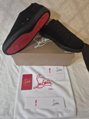 Svarta sneakers från Christian Louboutin - Snygga svarta sneakers från Christian Louboutin i mocka med klassisk röd sula. Lågt skaft, svarta skosnören och diskret design som ändå sticker ut tack vare den ikoniska röda undersidan. Perfekta för dig som gillar exklusiva detaljer och stilren look.