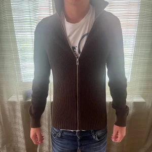 Brun stickad kofta från East West - East west zip brun. Skick 9,5/10 använd fåtal gånger. Modellen är 181 och väger 66, skriv vid frågor eller liknande!