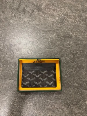 Svart kortfodral - Snyggt svart kortfodral med det klassiska vita och gråa mönstret. Tillverkat i canvas med läderdetaljer och har flera fack för kort. Kommer i originalask med gul insida och grönt lock. Perfekt för dig som vill ha något stilrent och exklusivt.