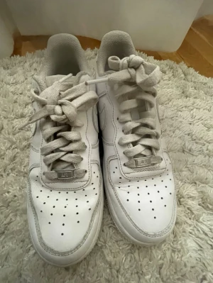 Vita Nike Air Force 1 sneakers - Klassiska vita Nike Air Force 1 sneakers i bra skicka. Skorna är använda ett få tal gånger då de är något stora på mig som vanligtvis har 41 i skor. Tillverkade i läder med diskret Nike märke på  sidan och metallbricka med 'AF1' på snörningen.