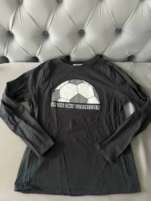 Svart långärmad tröja MANGO barn - Cool svart långärmad tröja med ett stort tryck av en fotboll från mango. Perfekt för dig som älskar fotboll och vill sticka ut på träningen eller i skolan. Mjuk och skön bomullskvalitet.