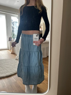 Ljusblå långkjol med volanger - Säljer en ljusblå långkjol med bred resår i midjan och flera volanglager. Kjolen har en avslappnad passform och är perfekt för vår och sommar. Materialet känns lätt och flowy, vilket gör den superbekväm att bära hela dagen.