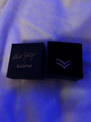 Alice stenlöf X guldfynd äkta silver ring - Snygg silvrig ring från Alice Stenlöf x Guldfynd med två V-formade band dekorerade med små gnistrande stenar. Ringen har en modern och trendig design som verkligen sticker ut. Perfekt accessoar för dig som gillar stilrena smycken med det lilla extra. Är inte helt säker på storleken men skulle gissa på runt 16/17. Använts ett fåtal gånger, inga skador eller dylikt. Så vitt som jag vet så går den ej att köpa längre. 