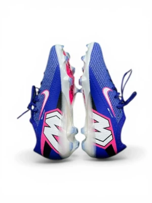 Nike blåa Mercurial fotbollsskor - Snygga blåa Nike Mercurial fotbollsskor med rosa och vita detaljer samt stor vit M-logga på sidan. Skorna har en modern, strömlinjeformad design med snörning och ovandel i syntetiskt material för bra grepp och kontroll på planen. Sulan är genomskinlig med dobbar för optimalt fäste.