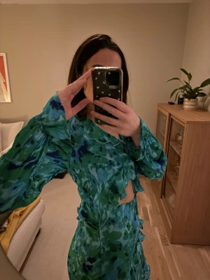 Mönstrad klänning med volang och knytning  - Superfin klänning i tunt material utan att bli genomskinlig. Har fina volangdetaljer och knytning vid bröstet. Slits, går till 3/4 av vaden på mig(170cm). Säljer pga felköp, aldrig använd. Blev fel storlek! Se sista bilden för rättvis bild på färgerna. Köpt på Boohoo.