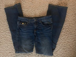 Mörkblå low waist bootcut jeans med fina fickor  - Mörkblåa jeans, bootcut, low waist, med knapar på bakfickorna från Gina i bra skick som inte passar mig längre.