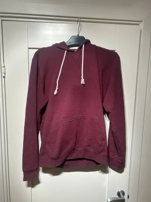 Vinröd hoodie med vita snören från pier one - Säljer en vinröd hoodie med klassisk ficka och vita dragsnören i huvan. Hoodien har långa ärmar och ribbade muddar vid ärmslut och nederkant. Perfekt för en avslappnad stil och enkel att matcha med jeans eller joggers.