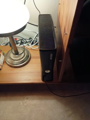 Xbox 360 Slim svart spelkonsol - Säljer en svart Xbox 360 Slim från Microsoft. Konsolen har en stilren, blank finish och är tillverkad i plast. Perfekt för gaming med vänner eller solo, och passar snyggt in i tv-möbeln. Strömkabel och HDMI-port finns på baksidan.
