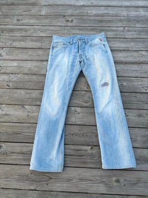 blå bootcut jeans från replay med snygg lagning  - Säljer ett par ljusblå replay waitom jeans med bootcut passform och slitna detaljer. Jeansen har en patchad lagning på ena benet och klassiska fem fickor. W32 L32    (DM om ni vill ha liknande lagning) 